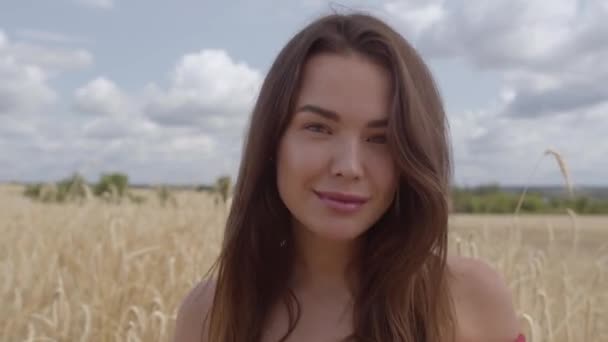 Hermosa mujer despreocupada disfrutando de la naturaleza y la luz del sol en el campo de trigo en el sol colorido increíble. Linda chica confiada mirando la cámara. Serie de personas reales . — Vídeo de stock