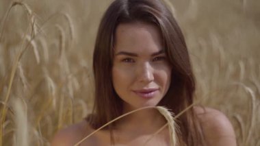 Portre büyüleyici kadın inanılmaz renkli güneş ışınları buğday alanında doğa ve güneş ışığı zevk. Sevimli kendine güvenen kız kameraya bakıyor. Gerçek insanlar serisi. Yavaş çekim.