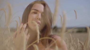 Portre büyüleyici genç kadın inanılmaz renkli güneş ışınları buğday alanında doğa ve güneş ışığı zevk. Sevimli kendine güvenen kız saç düzleştirmek ve kamera bakıyor. Gerçek insanlar serisi. Yavaş çekim.