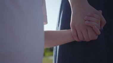 Eski kız kardeş ve küçük kardeş güneş ışığında yaz parkında eller tutarak yakın çekim. Açık havada boş zaman. Kardeşler arasındaki dost ilişkileri