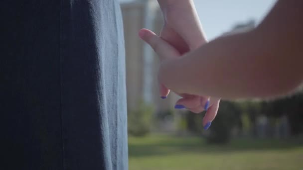 Close-up manos niña mayor y niño más joven tomados de la mano en el parque de verano a la luz del sol. Ocio al aire libre. Relaciones amistosas entre hermanos . — Vídeo de stock