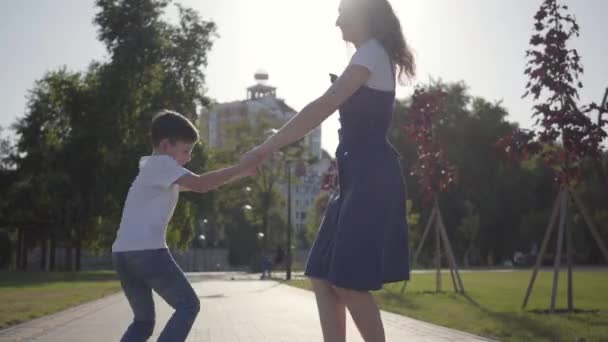 Sorella maggiore che gira con il fratello minore che si tiene per mano nel parco estivo. Tempo libero all'aperto. Rapporti amichevoli tra fratelli. Bambini spensierati che si divertono insieme — Video Stock