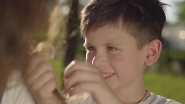 Retrato da irmã mais velha passar tempo com o irmão mais novo ao ar livre. O rapaz a tocar no cabelo da rapariga no parque. Lazer de verão — Vídeo de Stock