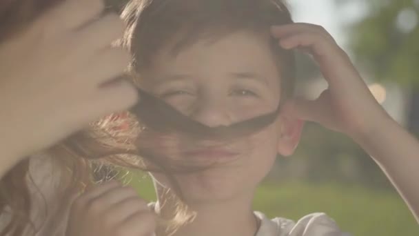 Retrato de close-up da irmã mais velha passar tempo com o irmão mais novo ao ar livre. O menino e a menina que fazem bigodes falsos com o cabelo da menina no parque. Lazer. Os irmãos se divertem juntos — Vídeo de Stock