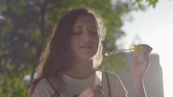 Το πορτρέτο της εφηβικής κοπέλας στο πάρκο που ανατινάζει φούσκες στην κάμερα. Χαριτωμένο νεαρή γυναίκα που περνά χρόνο μόνος σε εξωτερικούς χώρους. Θερινή αναψυχή — Αρχείο Βίντεο