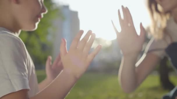 Older sister spending time with younger brother outdoors. The boy and girl playing pat-a-cake sitting on the blanket in the park. Summer leisure. — Stock Video