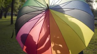 Çok renkli şemsiye ile çekici genç kız parkta küçük kardeşi öpüyor. Yaz tatilinde. Mutlu kardeşler açık havada eğlenmek