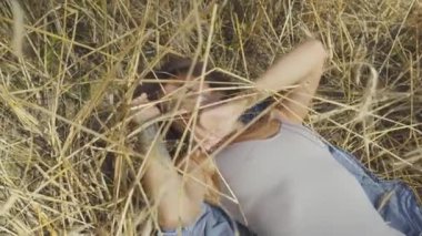 Buğday alanında saman üzerinde yatan çekici kadın kameraya bakıyor. Kız dışarıda dinleniyor. Doğa, doğal güzellik, kırsal yaşam tarzı ile bağlantı. Hasat süresi