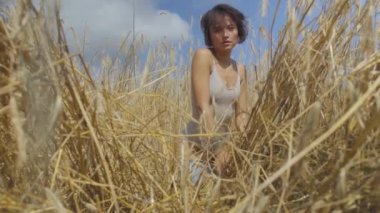 Kısa saçlı, buğday alanında rahatlatıcı bodysuit giyen zarif kadın. Kız kamera görünümlü ve poz doğa sahiptir. Kendine güvenen kaygısız kız açık havada. Gerçek insanlar serisi