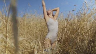 Kısa saçları olan şık kadın, buğday alanında rahatlatıcı bodysuit giyiyor. Kız kamera görünümlü ve poz doğa sahiptir. Kendine güvenen kaygısız kız açık havada. Gerçek insanlar serisi