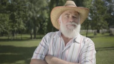 Park ayakta gülümseyen kamera bakıyor saman şapka emin eski gri sakallı adam. Açık havada boş zaman. Olgun adam yaz bahçesinde istirahat. Sağlıklı neşeli kıdemli emekli adam