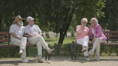 Parlak giyim ve erkek arkadaşları yaz parkında birbirlerine yakın tezgah üzerinde oturan iki kıdemli kız. Olgun insanlar açık havada dinleniyor. Neşeli kıdemli emekli insanlar.