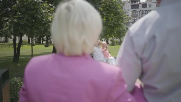 2つの愛らしい成熟したカップルが公園で会います。シニアカップルのダブルデート。おじい男女がお互いに挨拶し、男は握手をし、女性は抱き合う。元気な元気なシニア退職者. — ストック動画