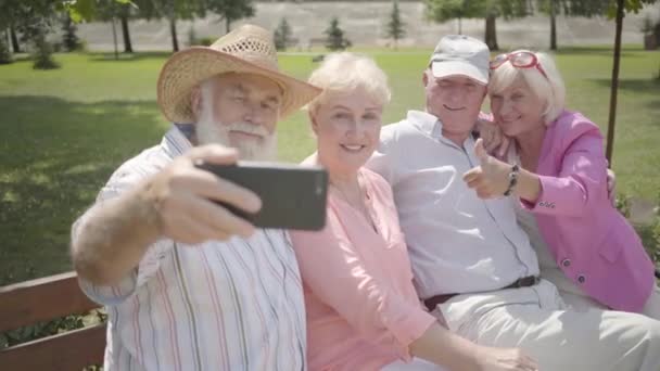 Dois adoráveis casais adultos de alegria sentados no banco juntos. O velhote a tirar uma selfie de companhia no parque. Pessoas maduras descansando ao ar livre. Lazer de verão. Cheerful idosos aposentados . — Vídeo de Stock