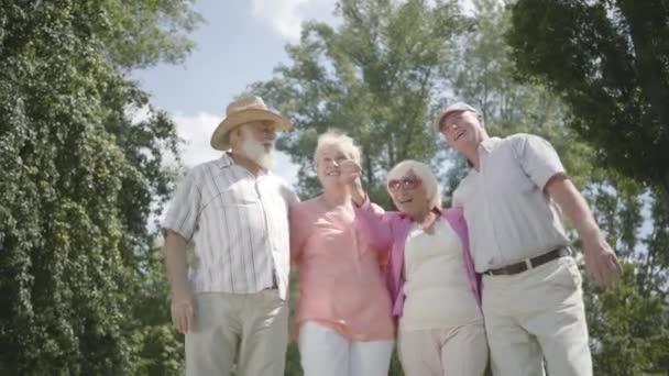 Due coppie mature sveglie guardando lontano in piedi nel parco insieme. Doppio appuntamento di coppie anziane. Compagnia amichevole che riposa all'aperto. Vecchi e vecchie che ridono felici. Rallentatore . — Video Stock