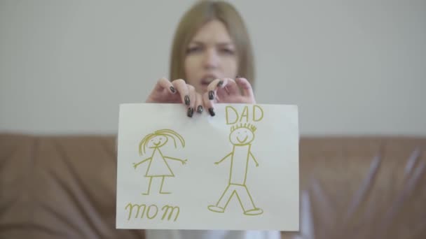 Portrait of sad young woman tearing apart childrens drawing with the image of mom and dad. Problems in the relationship between man and woman. Betrayal, mistrust, breakup concept. — Stock Video