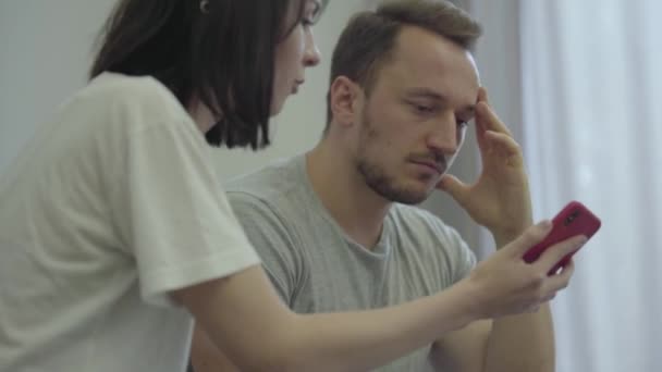 Portret van boze vrouw schreeuwen naar haar trieste man tonen mobiele telefoon met berichten van zijn minnaar thuis. Problemen in de relatie tussen man en vrouw. Verraad, wantrouwen, break-up concept — Stockvideo