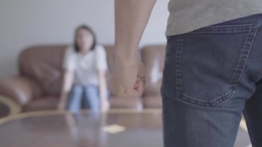Genç korkmuş kadın arka planda kanepede korku ile cringed iken tanınmaz adam ön planda öfke ile yumruklarını sıkmak. Aile içinde yanlış anlama.