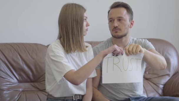 Мужчина и женщина разрывают на части слово доверие, написанное на бумаге. Проблемы в отношениях между мужчиной и женщиной. Предательство, недоверие, концепция расставания — стоковое видео