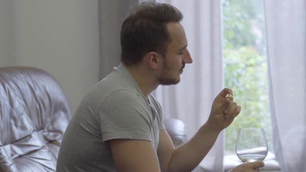 Retrato del hombre feliz sosteniendo anillo de bodas de oro y copa de vino sonriendo sentado en casa. El chico va a hacer una propuesta para su novia o recuerda los momentos agradables de la vida familiar . — Vídeos de Stock