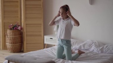 Modern ev oturma odasında yatakta müzik dinlerken kulaklıklar ile komik sevimli küçük kız. Evde müzik ile eğlenmek genç müzik sevgilisi. Carefree çocuk