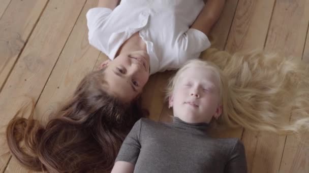 Zwei Freundinnen, die auf dem Holzboden liegen und einander anschauen. Konzept der Freundschaft. Unbeschwerte Kindheit. Serie "echte Menschen". — Stockvideo