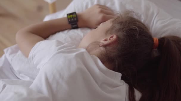 Linda niña durmiendo en la cama en casa. Adorable chica despertando de un despertador en su reloj inteligente. Tecnología moderna. Niñez despreocupada — Vídeos de Stock