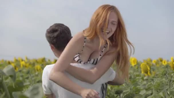 Mooie gelukkige paar op de zonnebloem veld. De jonge man gooit een meisje op zijn schouder, ze lacht. Jonge mensen die plezier hebben in de buitenlucht. Verbinding met de natuur. — Stockvideo