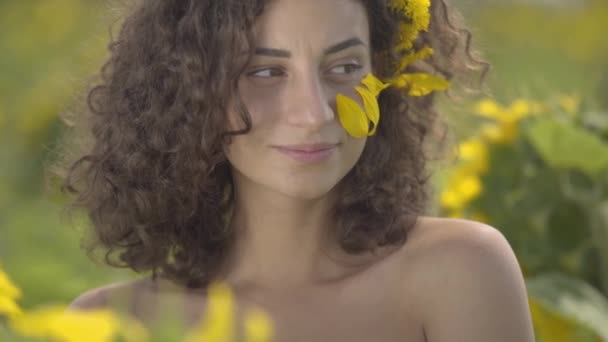 Retrato de chica juguetona bastante rizada y confiada mirando a la cámara sonriendo de pie en el campo de girasol. Color amarillo brillante. Concepto de libertad. Mujer feliz al aire libre. Movimiento lento . — Vídeos de Stock