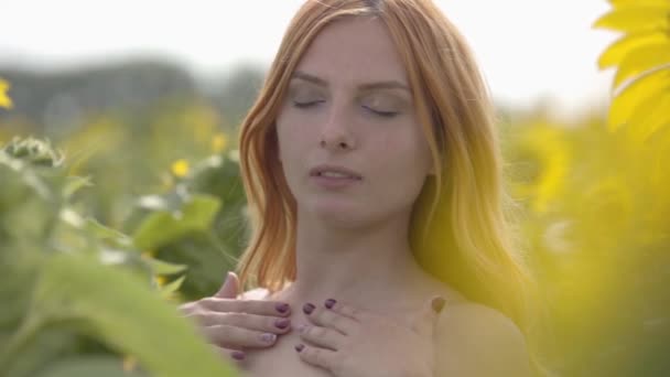 Portrait of confident sensual woman with red hair and green eyes standing on sunflower field. Concept of beauty, connection with nature. Freedom concept. Happy woman outdoors. Slow motion. — Stock Video