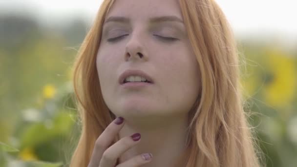 Portrétní portrét nádherné, sebevědomé dívky s červenými vlasy a zelenými očima na slunečnicovém poli. Pojem krásy, souvislost s přírodou. Zpomaleně. — Stock video