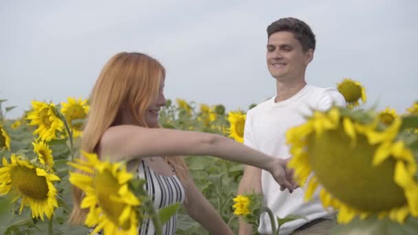 Mooie gelukkige paar dansen samen op de zonnebloem veld. Gember meisje met haar vriendje rust buitenshuis. Verbinding met de natuur. Freedom concept. Gelukkige tieners buitenshuis. Slow Motion — Stockvideo