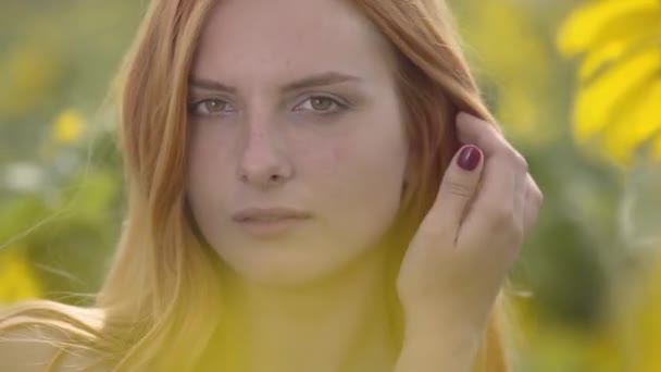 Close-up portret van zelfverzekerd sensueel meisje met rood haar en groene ogen staande op zonnebloem veld kijken naar camera. Concept van schoonheid, verbinding met de natuur. — Stockvideo