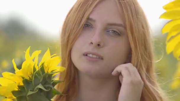 Porträtt av bedårande säker sensuell tjej med rött hår och gröna ögon stående på solrosfält tittar på kamera. Begreppet skönhet, samband med naturen. Frihets koncept. Lycklig kvinna Utomhus — Stockvideo