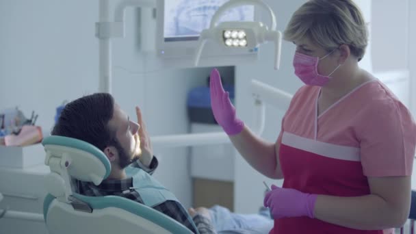 Dentista en máscara médica y guantes comprobando el estado de su paciente usando gestos. Médico estomatólogo profesional femenino en el trabajo. Tratamiento dental, concepto médico. Cuidado dental . — Vídeo de stock