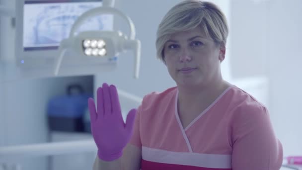 Donna dentista in un guanto medico sul posto di lavoro nello studio dentistico mostra gesti guardando la fotocamera. Medico professionista femminile stomatologo sul lavoro. Trattamento dentale, concetto medico . — Video Stock