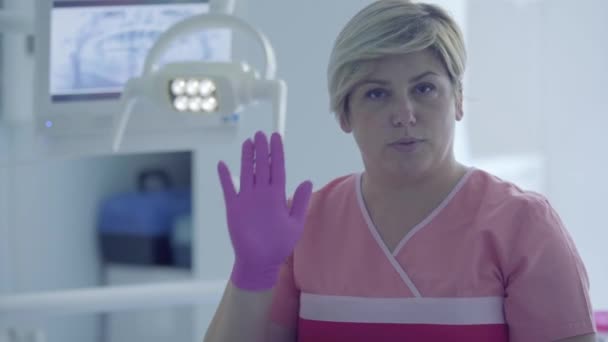 Carina dentista donna in un guanto medico sul posto di lavoro nello studio dentistico mostra gesti guardando la fotocamera. Medico professionista femminile stomatologo sul lavoro. Trattamento dentale, concetto medico . — Video Stock