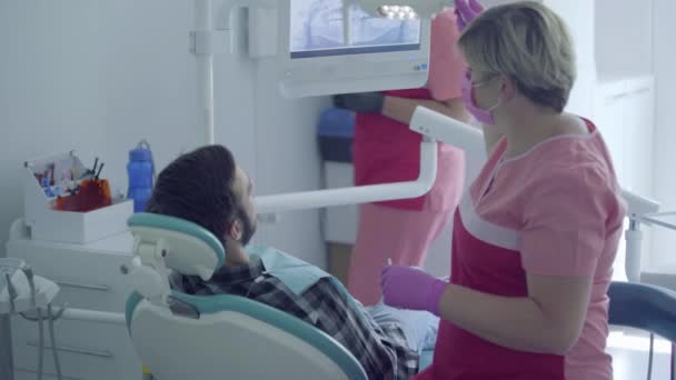 Dentist in medical mask and gloves checking the mouth of the patient using a mirror. Assistant bringing the instrument to doctor. Stomatologist at work in the office. Dental treatment, medical concept — Stock Video