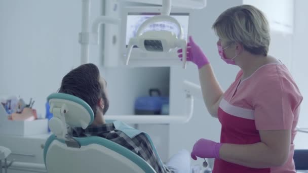 Tandläkare i medicinsk mask och handskar kontrollera patientens mun med hjälp av medicinska verktyg i en modern tandvård kontor. Kvinnlig professionell doktor tandläkare på jobbet. Tandbehandling, medicinskt koncept. — Stockvideo