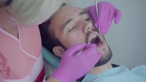 Стоматолог у медичній масці та рукавичках перевіряє рот пацієнта за допомогою медичних інструментів. На роботі працює професійний лікар стоматолог. Стоматологічне лікування, медична концепція. Стоматологічна допомога . — стокове відео