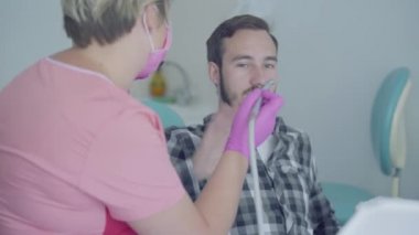 Tıbbi maske ve eldiven bayan diş hekimi tıbbi aletler kullanarak hastanın dişlerini kontrol etmeye hazır. Hasta korkuyor ama doktor adama güven tazeledi. Diş tedavisi, tıbbi kavram.