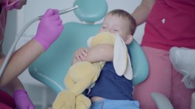 Tıbbi maske ve eldiven diş hekimi sandalyede oturan küçük kaygısız çocuk dişlerini kontrol etmeye hazır. Doktorla oynayan yaramaz çocuk. Diş tedavisi, tıbbi kavram.
