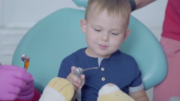 Malý bezstarostného chlapce, který sedí v křesle na zubařské pracovně. Roztomilá dětská hračka. Zubní péče, lékařská koncepce. — Stock video