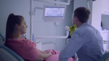 Tıbbi maskeli genç adam ekranda onun alt ve üst çeneleri onun kadın hasta resmi gösteren. Dişçiyi ziyaret eden kadın. Diş tedavisi, tıbbi konsept. Diş bakımı.