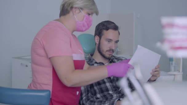 Femmina dentista i maschera medica e guanti che mostrano a immagine paziente maschile dei suoi denti. Il giovanotto che va dal dottore. Cure dentali, concetto medico. Cure dentali . — Video Stock