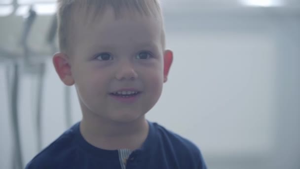 Portré egy aranyos vicces mosolygó fiú mutatja hüvelykujját felfelé nézi a kamerát. Gondtalan gyermek látogató orvos. — Stock videók