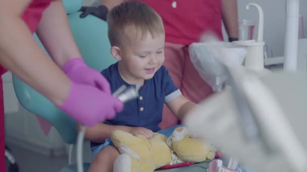 Bedårande liten pojke leker med medicinska verktyg sitter i stolen i tandläkar byrån. Bekymmerslöst barn som besöker läkare. Pojken spelar hos tandläkaren. Tandbehandling, medicinskt koncept. Tandvård. — Stockvideo