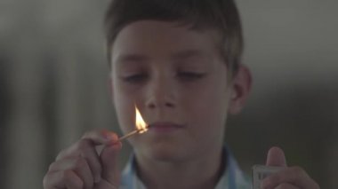 Karanlık dumanlı odada kibritile oynayan yakın portre sevimli küçük çocuk. Çocuk maçı gülümseyerek yaktı. Çocuk ateşle oynuyor. Kundakçılar