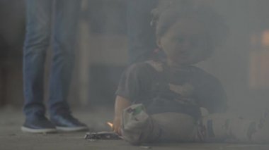 Duman bulutunun içinde karanlık odada tanınmayan iki çocuk. Korkunç kirli bebek ön planda yerde yanıyor. Yangın kavramı, yanıcılık, güvenlik kurallarına uyulmaması