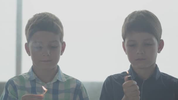 Dos hermanitos gemelos jugando con el fuego en la habitación humeante frente a una ventana. Niños sacando cerillas y cabezas más livianas y temblorosas. Los niños enseñan a no jugar con fuego. Concepto de peligro — Vídeo de stock